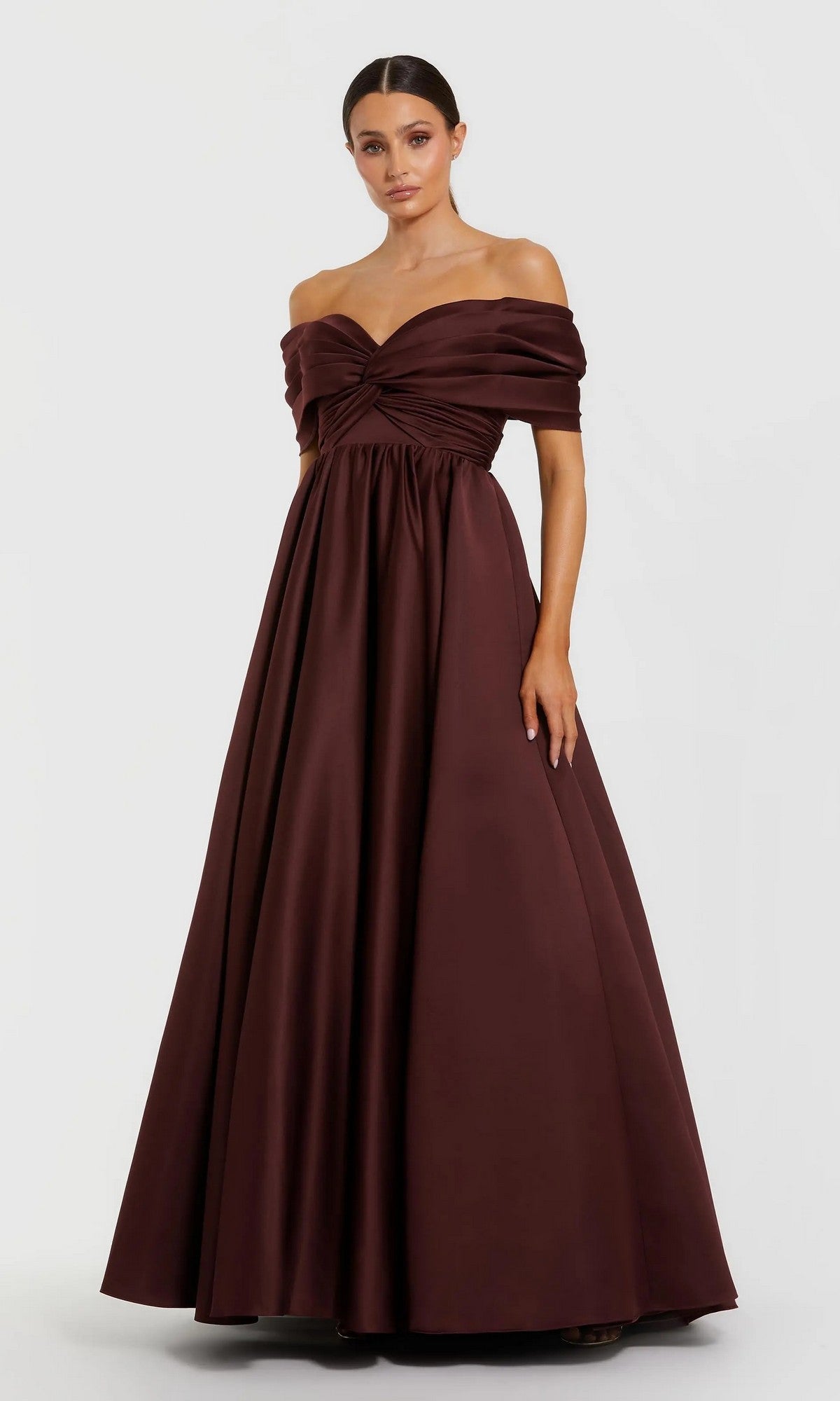 A woman in the Mac Duggal 56188 long formal dress—a floor-length, dark burgundy off-the-shoulder satin ballgown with a fitted bodice and full skirt—stands against a plain light background.